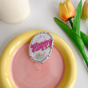 Detail eines glitzernden pinkfarbenen 'Happy' Handyhalters mit silbernem Hammerschlag