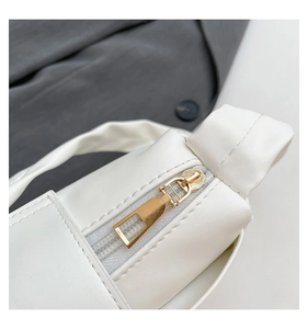 Close-up of golden zipper and stitching on a minimalist white pleated baguette bag