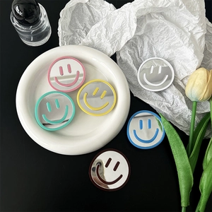 Cute smiley face mirror phone grip stand in six pastel colors on a stylish white tray