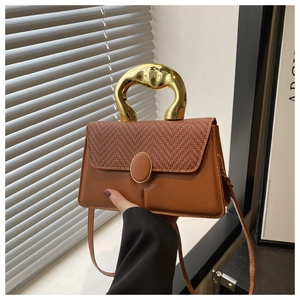 Detailed shot of brown leather bag with woven flap and artistic gold metal handle