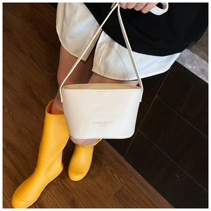 Close-up of white lychee grain bucket bag featuring fashion text and a slim shoulder strap