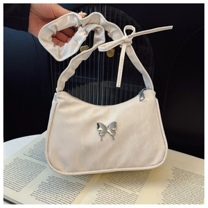 Detail of cream shoulder bag featuring silver metal butterfly and pleated drawstring strap
