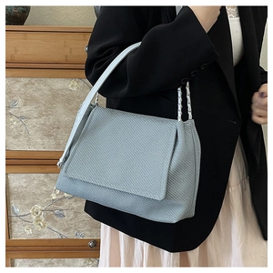 Detail of light blue textured shoulder bag with chain strap worn with casual outfit