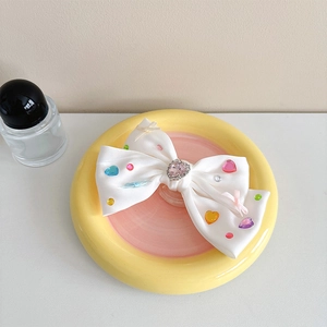 Detail of white satin bow hair clip with colorful heart rhinestones and a pink gemstone