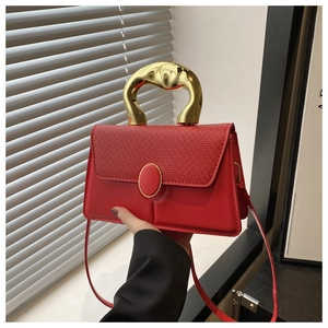 Detail of red crossbody bag with wave gold handle and textured woven leather flap