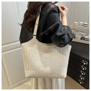 Detail of cream woven tote bag featuring a leather Fashion patch and shoulder strap