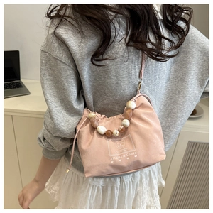 Detail of pink drawstring crossbody bag featuring marble-patterned beaded handle on shoulder