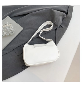 White pleated underarm bag detail on a grey suit with elegant lifestyle props
