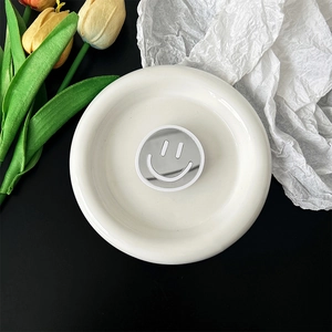 Detail of a portable smiley mirror phone grip holder on a white ceramic tray