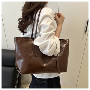 Detail of a large vintage brown tote bag in glossy faux leather worn by a model