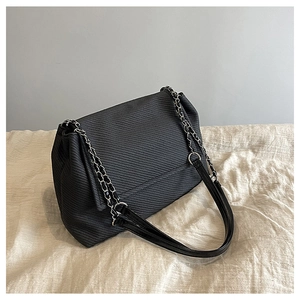 Detail of black twill textured flap bag showing fine weave and metal chain shoulder strap