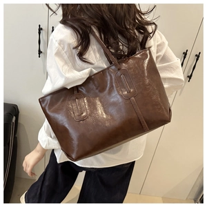 Detail of deep brown glossy tote bag showing textured stitching and shoulder strap