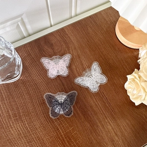 Lace butterfly phone grip stand in pink, white, and black on a dark wood table
