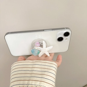 Detail of glitter starfish and seashell phone socket grip held on a smartphone