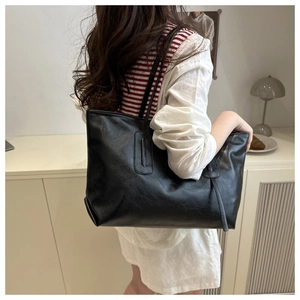 Side view of a large black faux leather tote bag worn by a model in a warm indoor setting