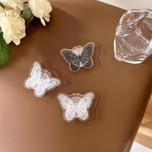 Lace butterfly acrylic phone grip stands in black and white on a leather surface