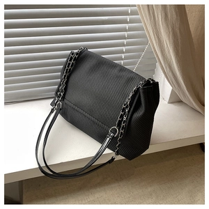 Detail of black corduroy shoulder bag with silver chain strap and flap closure design