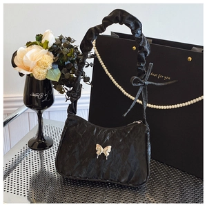 Detail of black ruched underarm bag featuring silver metal butterfly and bow handle