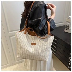 Detail of cream straw tote bag with brown leather handles and 'FASHION' patch