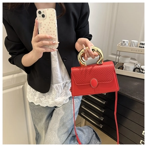 Detail of red crossbody bag with woven flap and large gold metal handle in lifestyle setting