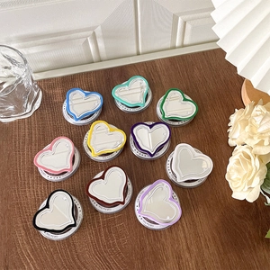 Magnetic MagSafe heart-shaped mirror phone grips in ten colors on a rustic wooden desk