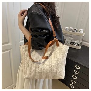 Detail of woven straw tote bag with brown leather handles and fashion logo patch