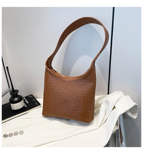 Detailed texture of brown woven hobo bucket bag styled on a white blazer background