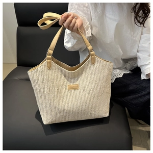 Detail of handwoven beige straw tote bag featuring leather handles and FASHION logo plaque