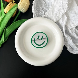 Detail of green smiley face phone grip with mirror finish on white tray with tulips