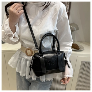 Detalle de bolso Boston negro con texto en relieve y hebillas plateadas puesto en modelo