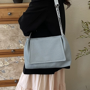 Minimalist light blue shoulder bag with chain strap and fine twill texture worn by model