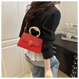 Detail view of red shoulder bag featuring textured flap and elegant gold metal handle