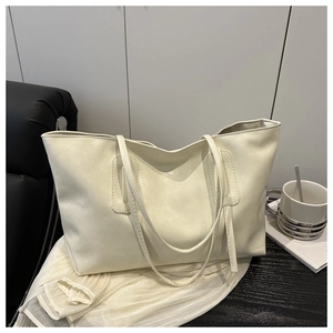 Detail of a large cream leather tote bag on a black leather sofa in a modern office