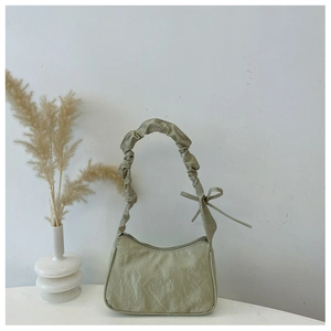 Detail of light green pleated shoulder bag with knotted bow handle on a white desk