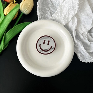 Close-up of a round smiley face mirror phone socket on a white decorative ceramic plate
