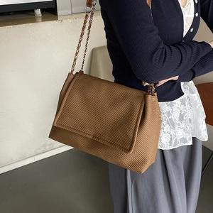 Brown textured shoulder bag with chain strap and flap closure shown on a model