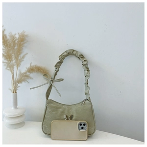 Detail of light green pleated shoulder bag featuring a silver butterfly charm and bow