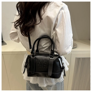 Sac Boston minimaliste en cuir noir porté en bandoulière et à la main par un mannequin