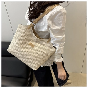 Detail of woven straw tote bag with brown leather handle and fashion tag on shoulder