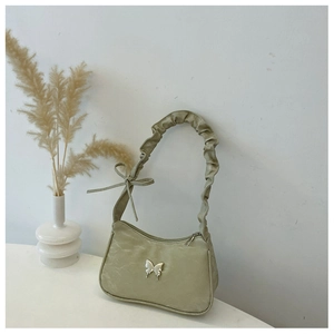 Detail of ruched shoulder strap and silver butterfly emblem on light green bag
