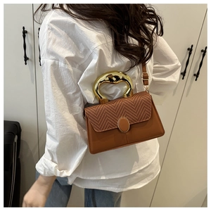 Brown leather handbag with woven flap and large gold metal handle worn by model