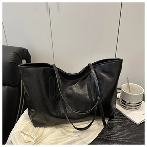 Detail view of large black tote bag with glossy leather texture on a wooden desk