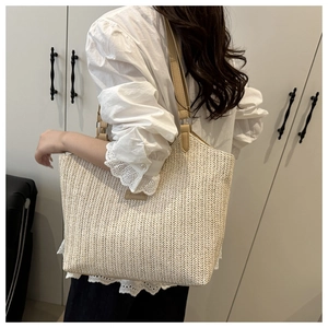 Detail of a cream woven straw tote bag featuring a leather patch and dual handles
