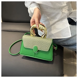 Detail view of green leather handbag with oversized gold metal handle and herringbone pattern