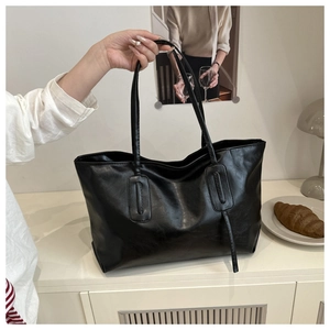 Close-up of a black high-gloss PU leather tote bag in a minimalist home setting