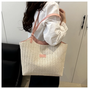 Detail of beige straw tote bag with pink leather strap and fashion label on shoulder