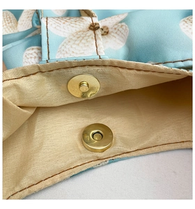 Close-up of metal magnetic buckle and floral fabric stitching on a minimalist shoulder bag