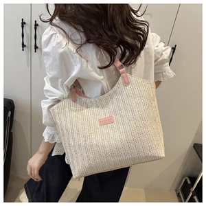 Détail du sac fourre-tout en paille beige avec poignée en cuir rose et écusson mode