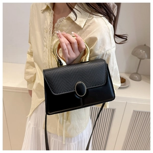 Detail of black crossbody bag with woven texture, gold hardware and horseshoe handle