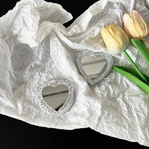 Close-up of heart-shaped glitter mirror phone stand on white aesthetic background